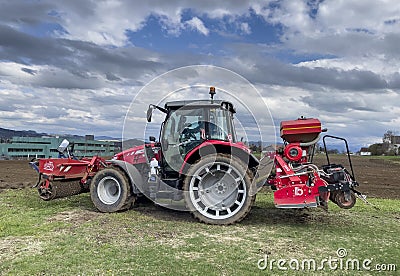 Tractor plows the field in front of some agricultural buildings on a sunny spring day Editorial Stock Photo