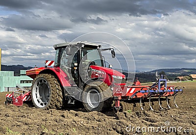 Tractor plows the field in front of some agricultural buildings on a sunny spring day Editorial Stock Photo