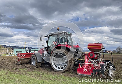 Tractor plows the field in front of some agricultural buildings on a sunny spring day Editorial Stock Photo