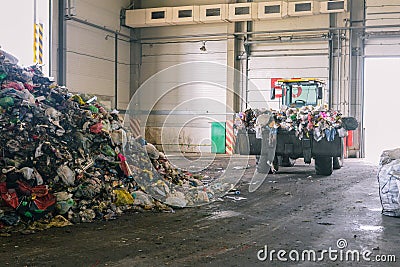 Tractor transports garbage at the plant for processing and sorting waste. Raised bulldozer bucket with waste. Pile of trash in the Stock Photo