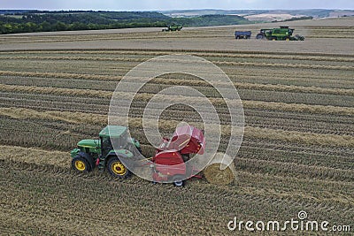 A tractor uses a trailed bale machine to collect straw in the field and make round large bales. Agricultural work, baling, baler, Editorial Stock Photo