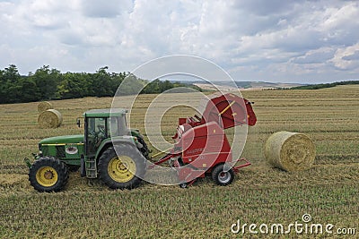 A tractor uses a trailed bale machine to collect straw in the field and make round large bales. Agricultural work, baling, baler, Editorial Stock Photo