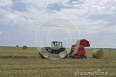 A tractor uses a trailed bale machine to collect straw in the field and make round large bales. Agricultural work, baling, baler, Editorial Stock Photo