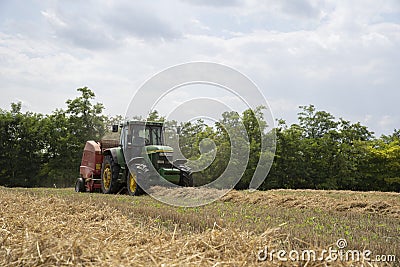 A tractor uses a trailed bale machine to collect straw in the field and make round large bales. Agricultural work, baling, baler, Editorial Stock Photo