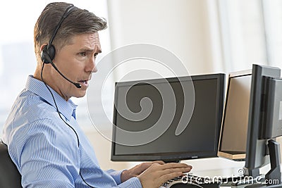 Trader Using Multiple Computer Screens While Communicating Through Headphones Stock Photo