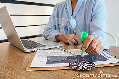 Trader woman holding a darts aiming at the target center of dart board, Setting challenging trading goals And ready to achieve Stock Photo