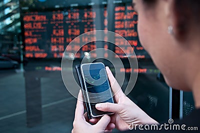 Trading stock on mobile near exchange board Stock Photo