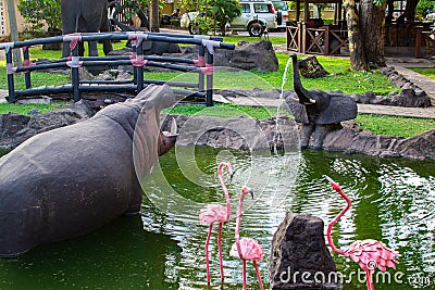 Traditional african handcrafted wooden statues of hipo, elephant and flamingo in a pond of the garden of Cultural Heritage store Editorial Stock Photo