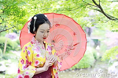 Traditional Asian Japanese beautiful Geisha woman bride wears kimono hold a red umbrella in a summer nature Stock Photo