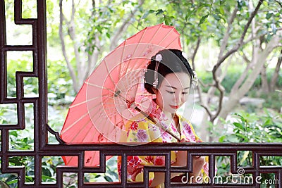Traditional Asian Japanese beautiful Geisha woman bride wears kimono with red umbrella on hand in a summer nature Stock Photo
