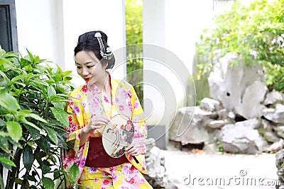 Traditional Asian Japanese beautiful woman wears kimono with fan on hand smiling playing on outdoor spring garden Stock Photo