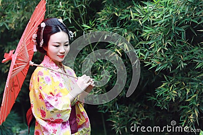 Traditional Asian Japanese bride with kimono hold a red umbrella stand by bamboo in a park Stock Photo