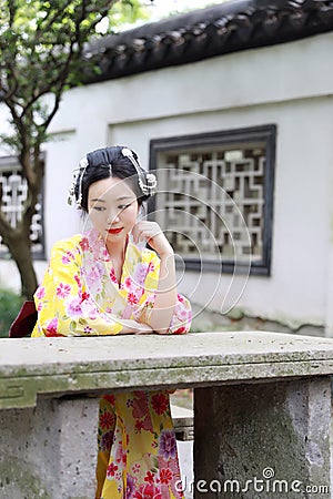 Traditional Asian Japanese woman in a outdoor garden sit on a stone bench Stock Photo