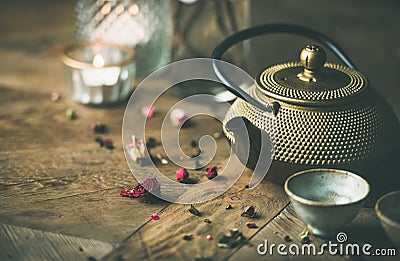 Golden iron teapot, cups, dried rose, candles over wooden background Stock Photo