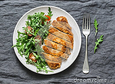 Traditional chicken schnitzel with arugula cherry tomatoes salad on grey background Stock Photo