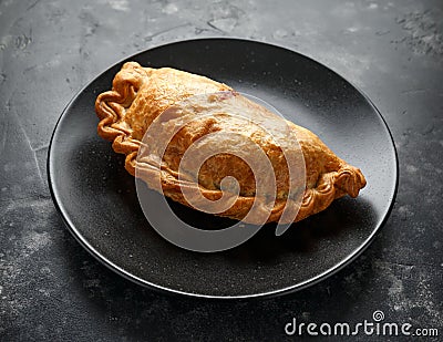 Traditional Cornish pasty filled with beef meat, potato and vegetables on black plate Stock Photo