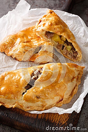 Traditional Cornish pasty filled with beef meat, potato and vegetables closeup on the paper. Vertical Stock Photo