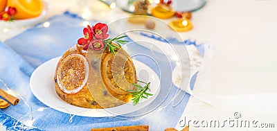 Traditional English Christmas pudding decorated with oranges and flowers in festive table setting with fruits and spices, blue Stock Photo