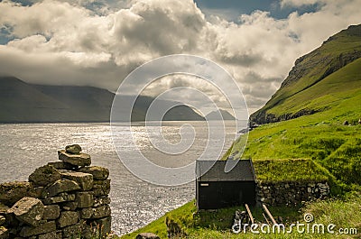 Traditional faroese shed ath the edge of the cliff, Mikladalur, Kalsoy, beautiful view on the sea and islands Kunoy and Bordoy, Stock Photo