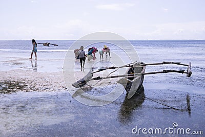 Traditional fishing boat on the coast of Zanzibar island in Tanzania. African woman picking seaweed in the back. Landscape view. Editorial Stock Photo