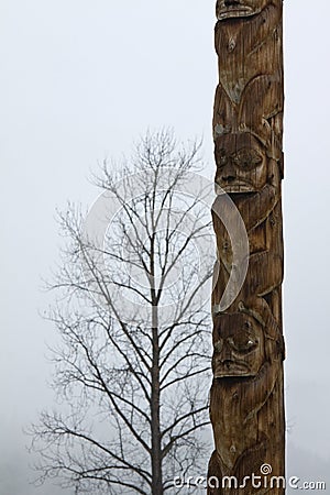 Traditional Gitxsan totem poles with lone tree behind Stock Photo