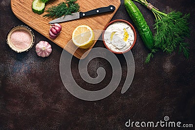 Traditional greek tzatziki sauce with ingredients on dark rustic background. Greek yogurt with cucumber, dill, garlic and lemon. Stock Photo