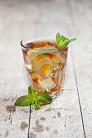 Traditional iced tea with lemon, mint leaves and ice in glass on rustic wooden table Stock Photo