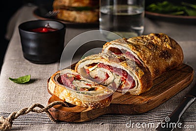 Traditional Italian Stromboli stuffed with cheese, salami, red pepper and spinach. Photo in a dark style. Stock Photo