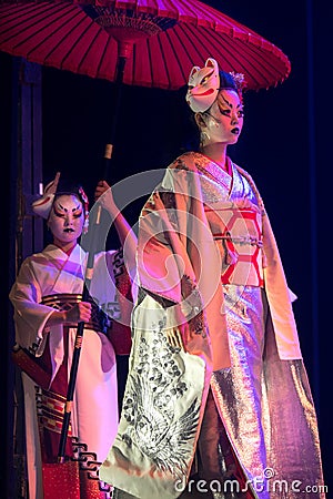 Actress in traditional kimono and fox mark gradually goes and her assistant holds umbrella above Stock Photo