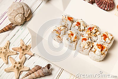 Japanese Volcano Sushi Roll pieces with raw scallop and Tobiko caviar on carton delivery takeaway box. white wooden background Stock Photo