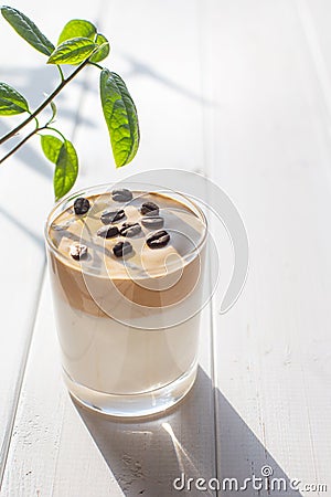 Traditional Korean milk drink with caffeine, Dalgona coffee in a glass with coffee beans on a background of white boards Stock Photo