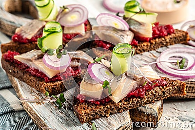 Traditional matie herring with beetroot salad, fresh cucumber and onion rings on the toasts on white plate. Scandinavian cuisine Stock Photo