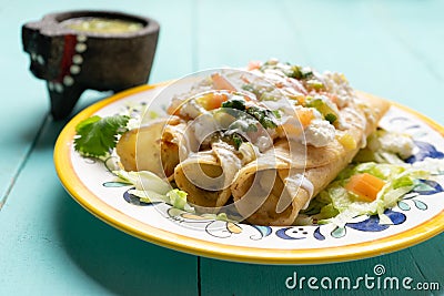 Mexican potato and cheese fried tacos also called flautas with green sauce on turquoise background Stock Photo