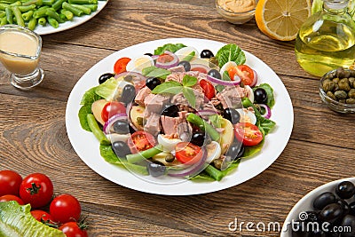 Traditional Nicoise salad in a white plate on an old rural table with sauce and ingredients. Selected focus. Stock Photo