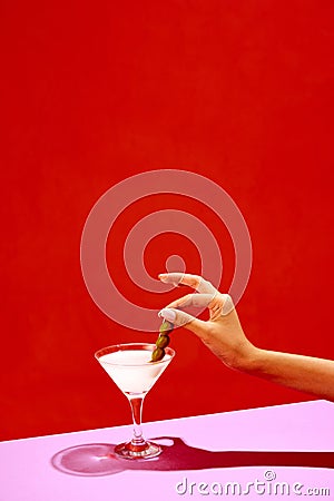 Traditional original drink. Glass with martini decorated with olives isolated over red background. Salty taste of Stock Photo