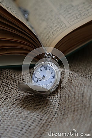 ancient pocket watch in front of an old book on a piece of cloth Stock Photo