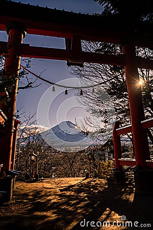 A traditional red torii gate and the Fuji mountain with snow cover at sunset Stock Photo