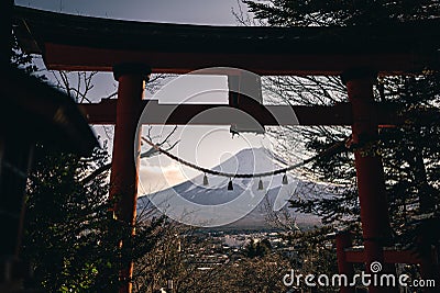 A traditional red torii gate and the Fuji mountain with snow cover at sunset Stock Photo