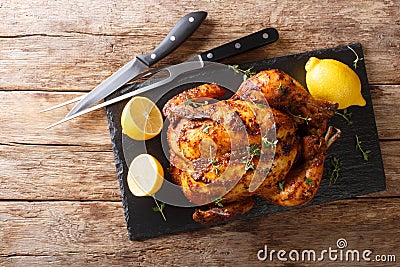 Traditional rotisserie chicken served with lemon closeup on a slate board on a table. Horizontal top view Stock Photo