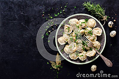 Traditional russian pelmeni, ravioli, dumplings with meat on black concrete background. Parsley, quail eggs, pepper Stock Photo