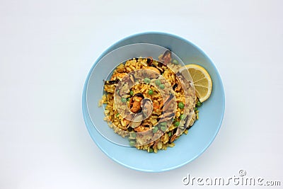 Traditional Spanish seafood dish paella with lemon slice on table. Mussel risotto with green peas on blue plate on white table Stock Photo