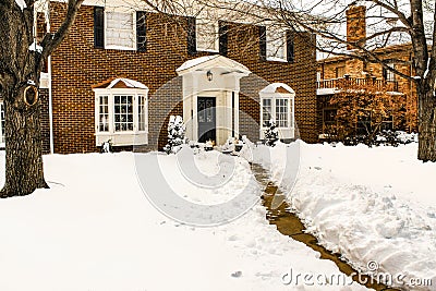 Traditional two story brick house with bay windows and pillared porch in the snow with the sidewalk cleared Stock Photo