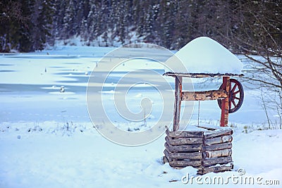Traditional water fountain covered in snow on the side of the frozen Lacul Rosu lake Stock Photo