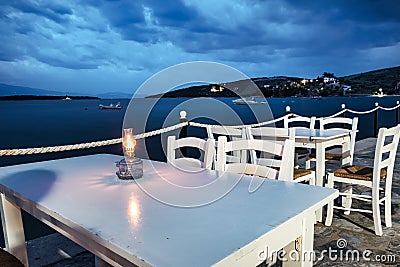 Traditional white wooden tables and chairs of a greek tavern at night and the view of the beach of Amaliapoli, Greece Stock Photo
