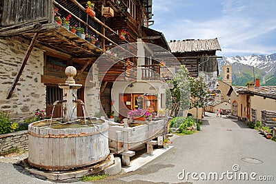 Traditional wooden houses, a traditional fountain and the church in Saint Veran village, with mountain range Editorial Stock Photo