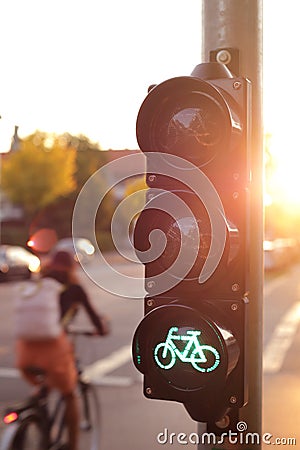 traffic light for a cycling lane showing green bicycle symbol in bright morning light with cyclist driving by in background Stock Photo