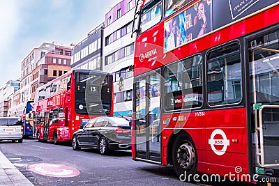 Traffic in London - two typical red buses with adverts, black mercedes, grey car. Editorial Stock Photo