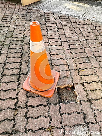 Traffic safety cone to warn missing paver bricks floor pathway. Selective focus. Stock Photo