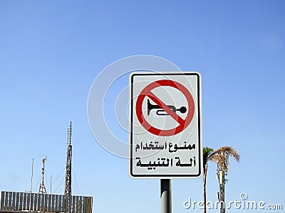 A traffic sign at the side of the road, Translation of the Arabic text (Car horn is not allowed), a forbidden zone area Stock Photo