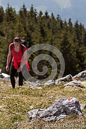 Trail marking on rock and female hiker ascending the mountain in background Stock Photo